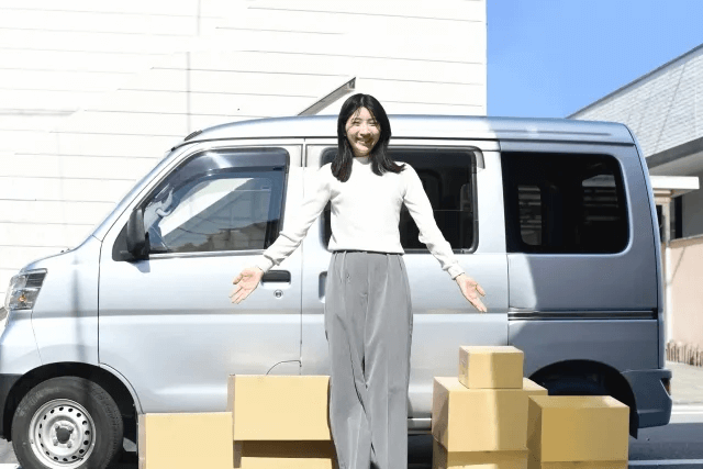 車と大量の段ボール箱の前に立つ若い女性