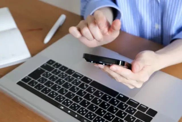 パソコンの前でスマホを操作してる女性