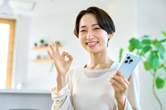 スマホを片手にOKサインを出してる笑顔の女性