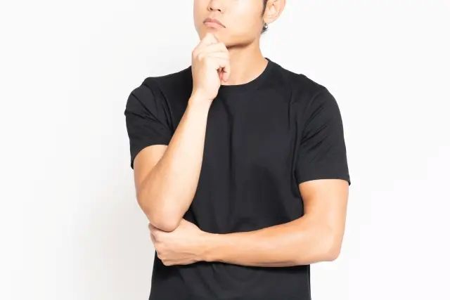 白い背景の前に立って、悩んでいる黒いTシャツを着ている男性
